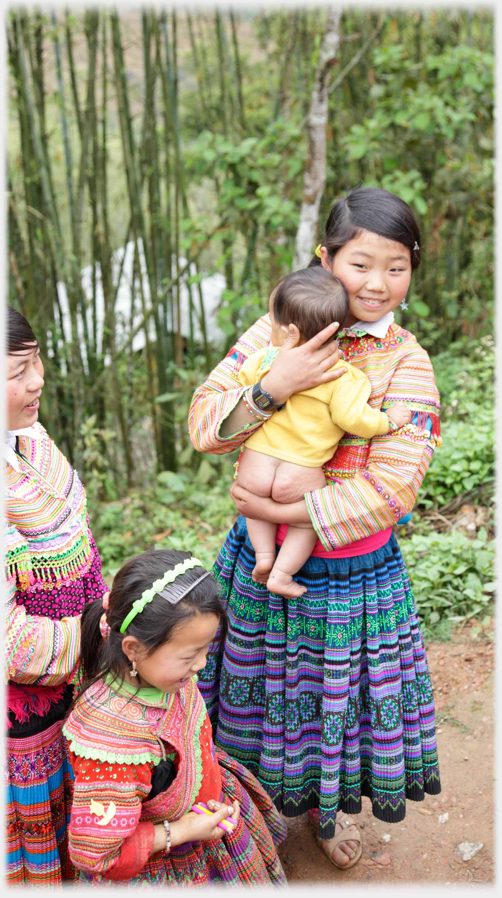 Hmong woman holding bare bottomed infant, beside girl.