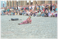 Man lying on cobbles with large crowd behind watching.