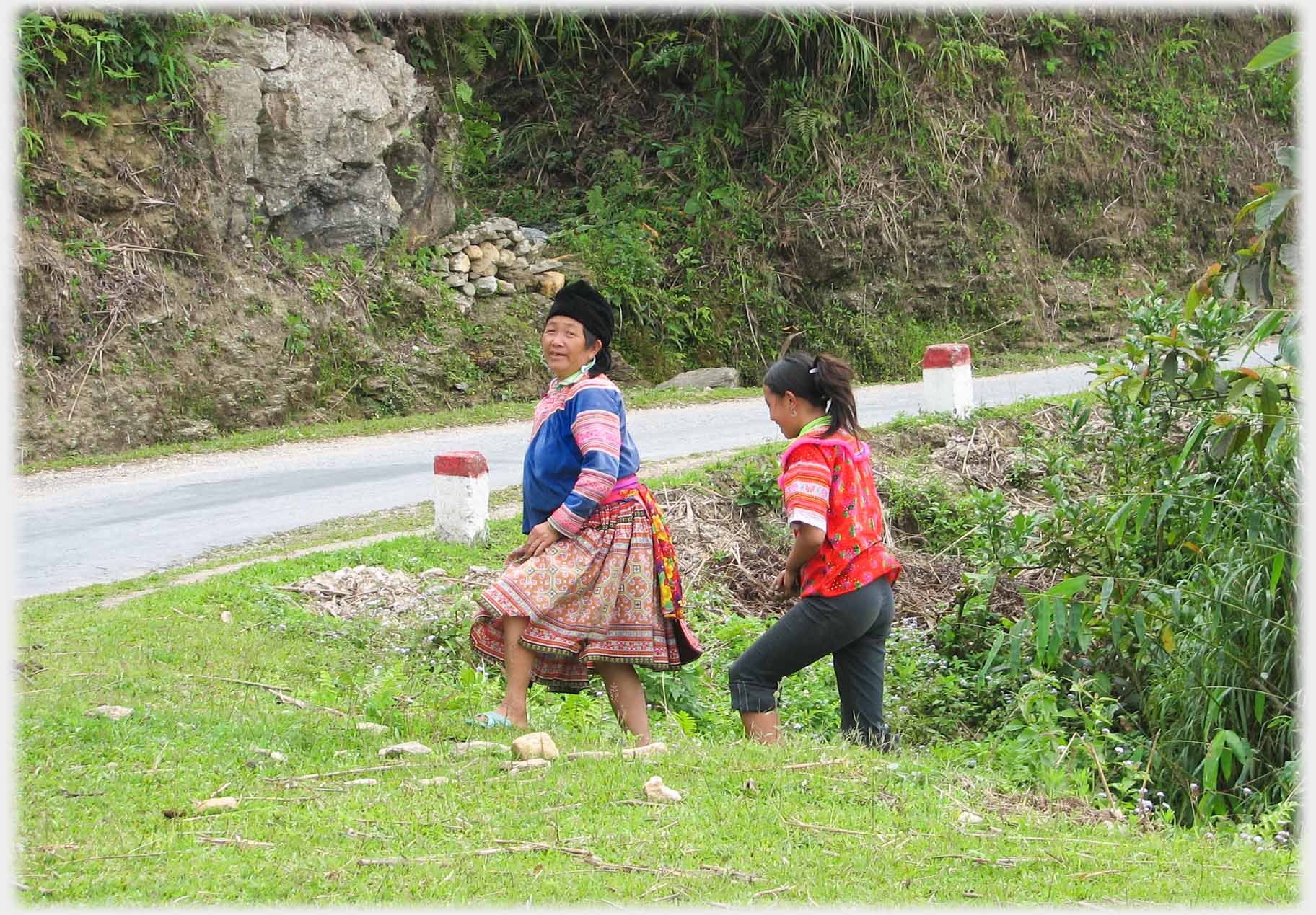 Two women walking up onto grassy roadside.