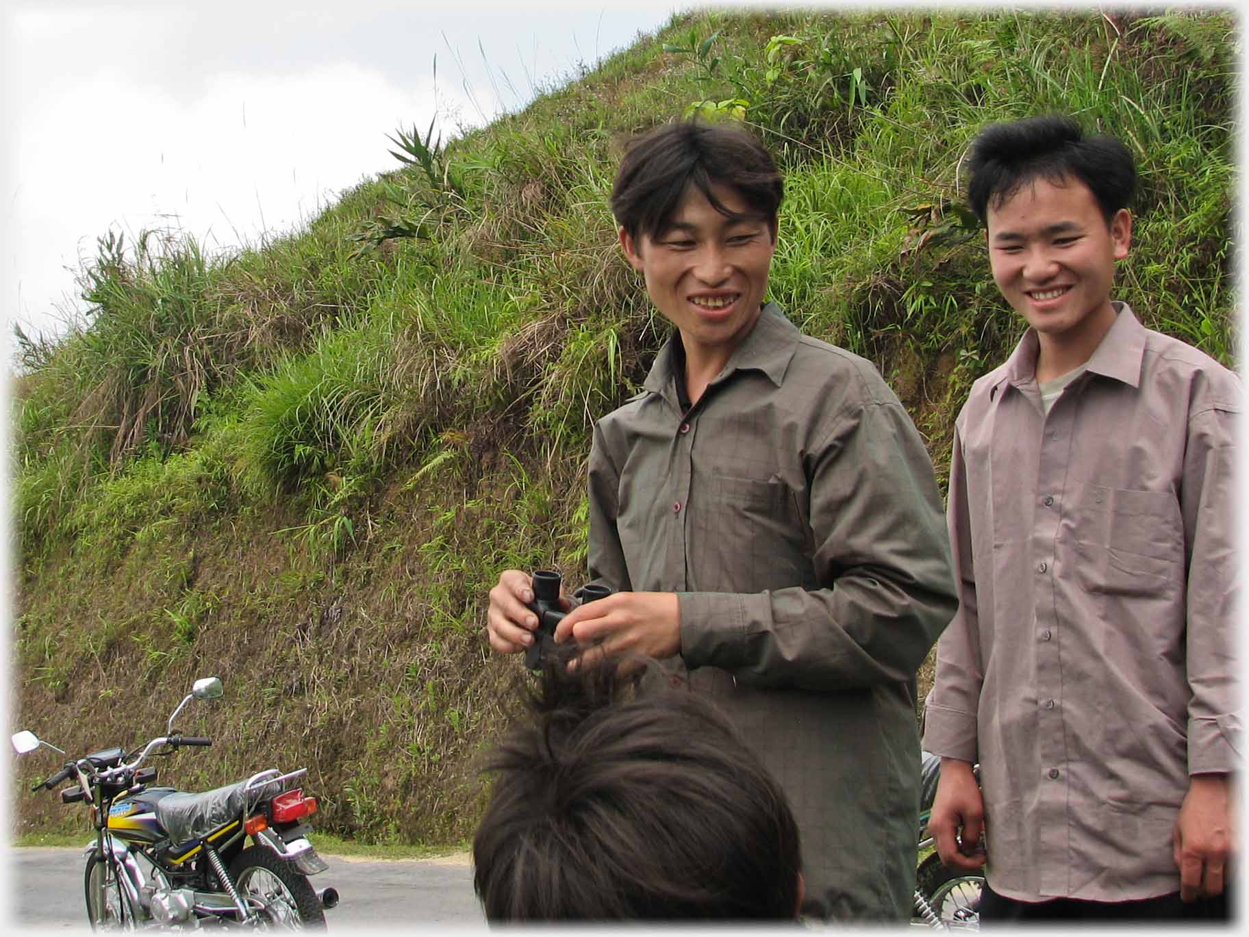 Two men talking to one below photo, one man holding binoculars.