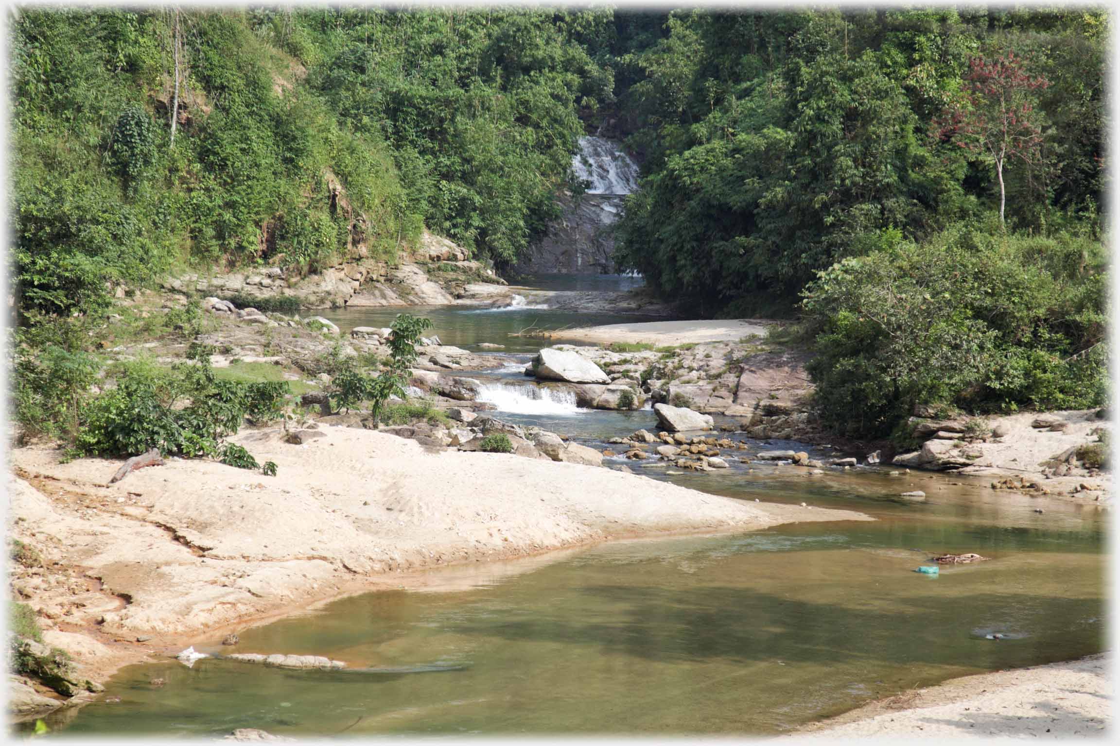 Small river winding between flat rocks, waterfall in distance.