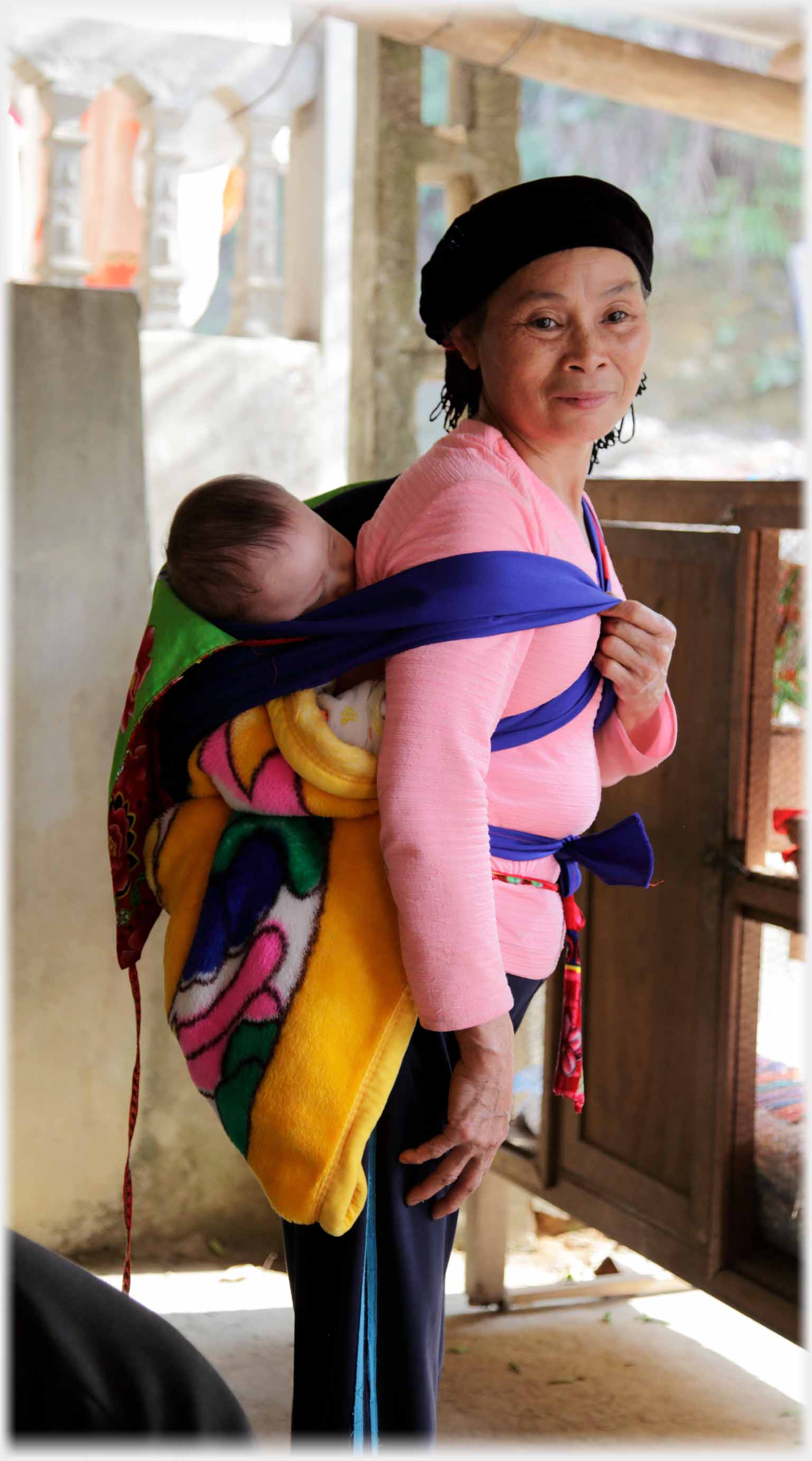 Woman with baby on her back standing looking at the camera.