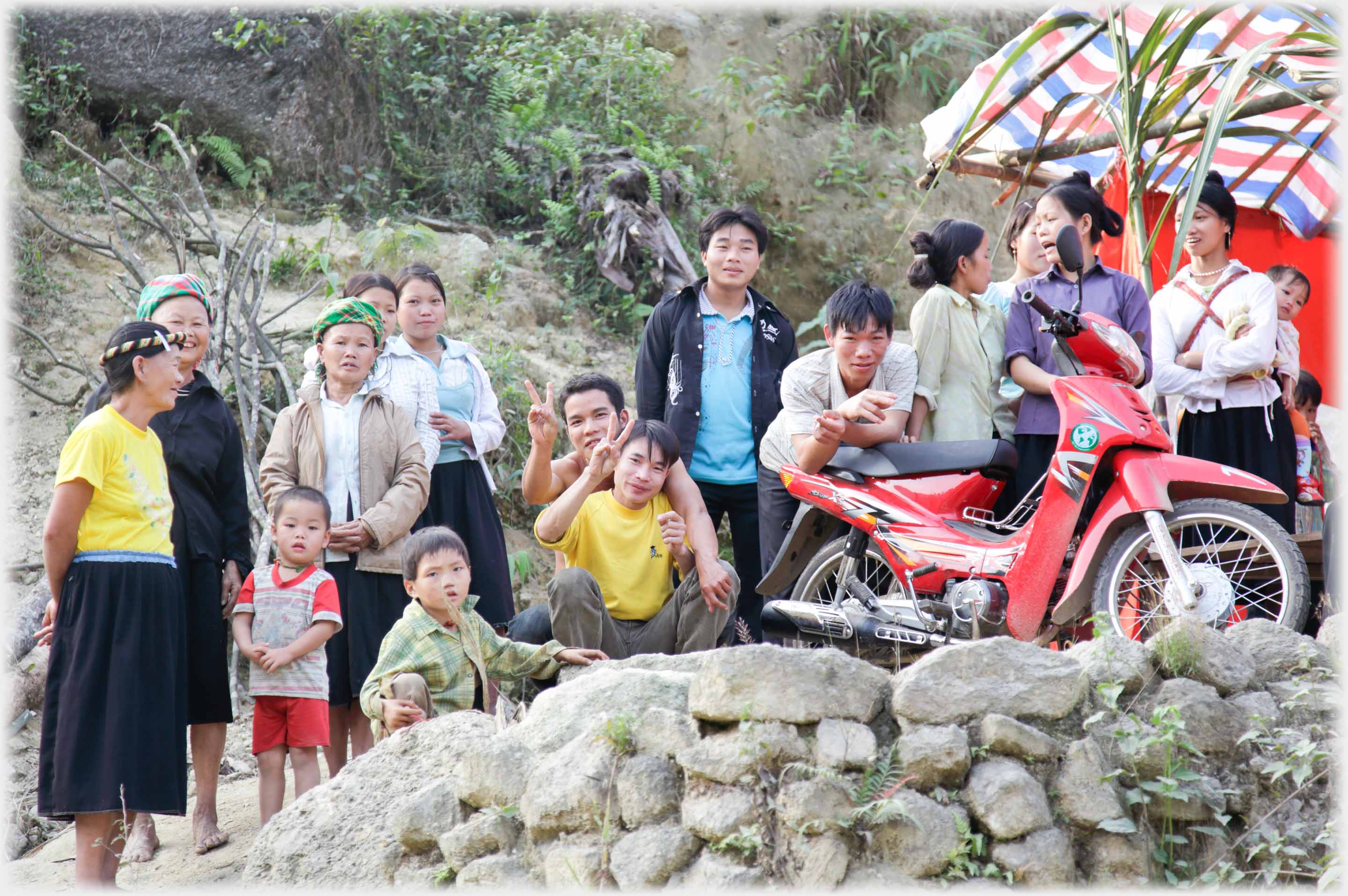 A dozen or more people grouped along wall by motorbike, some waving.