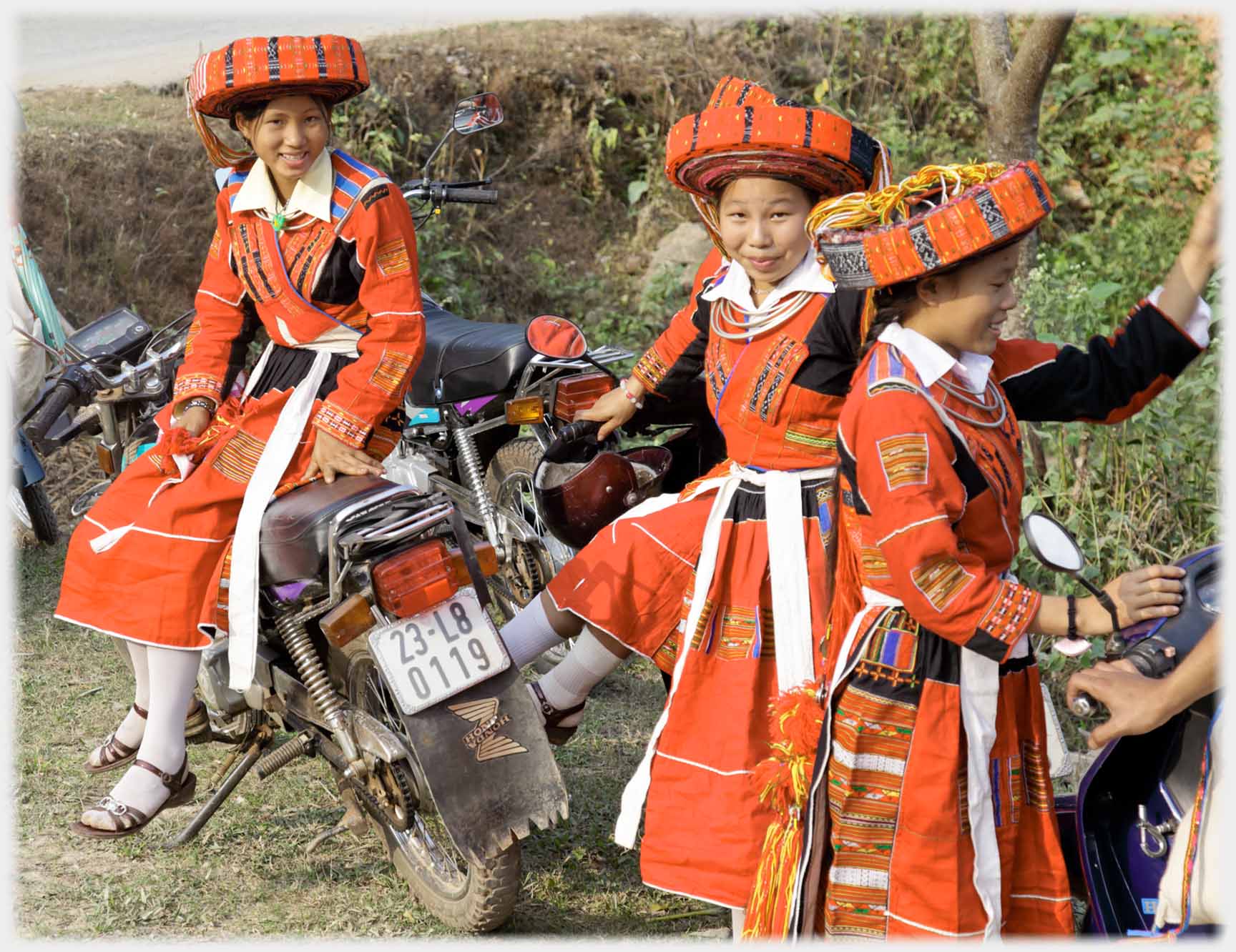 Three women in red clothes and hats on/by motorbikes.