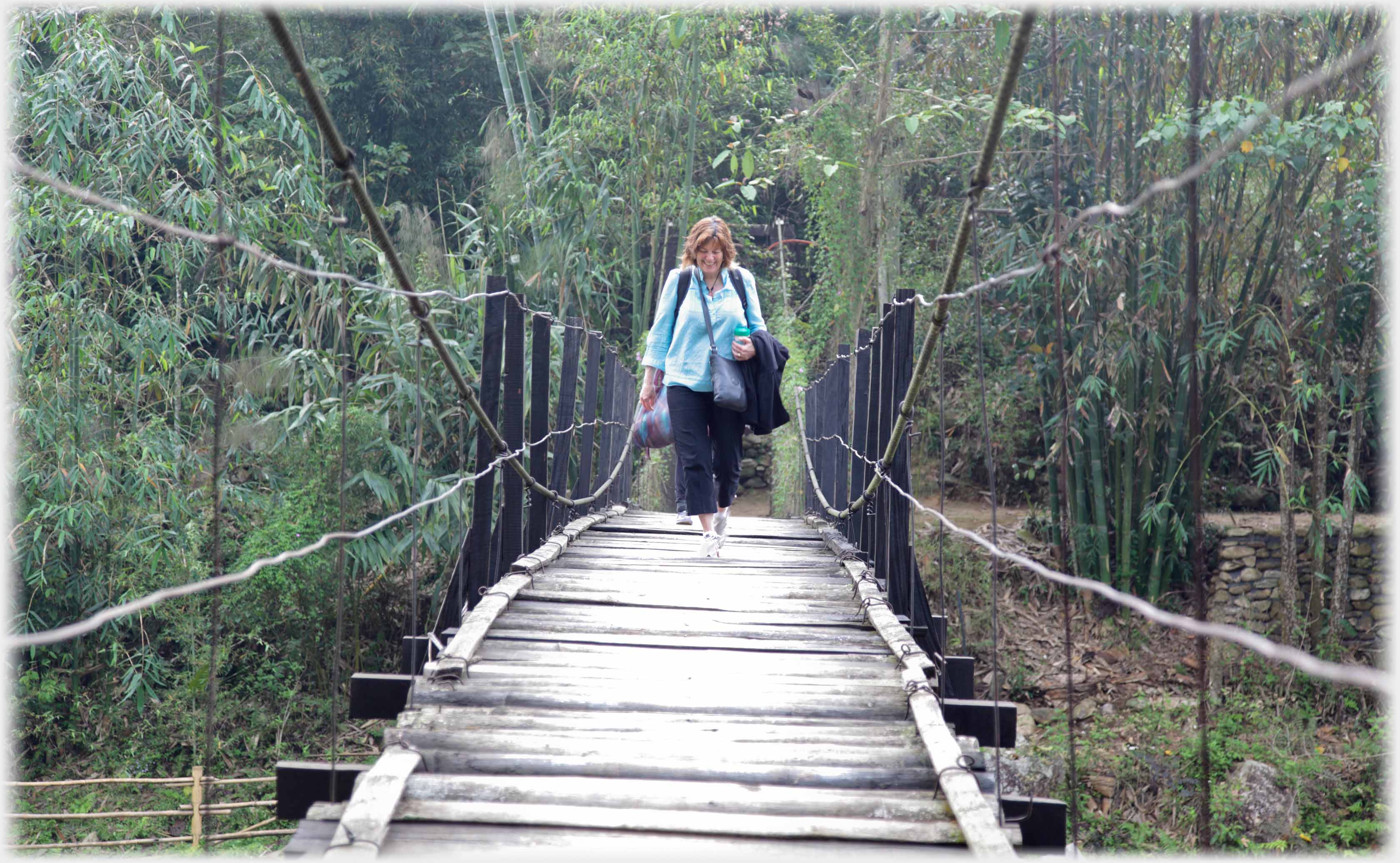 Woman walking towards camera on suspension foot-bridge.