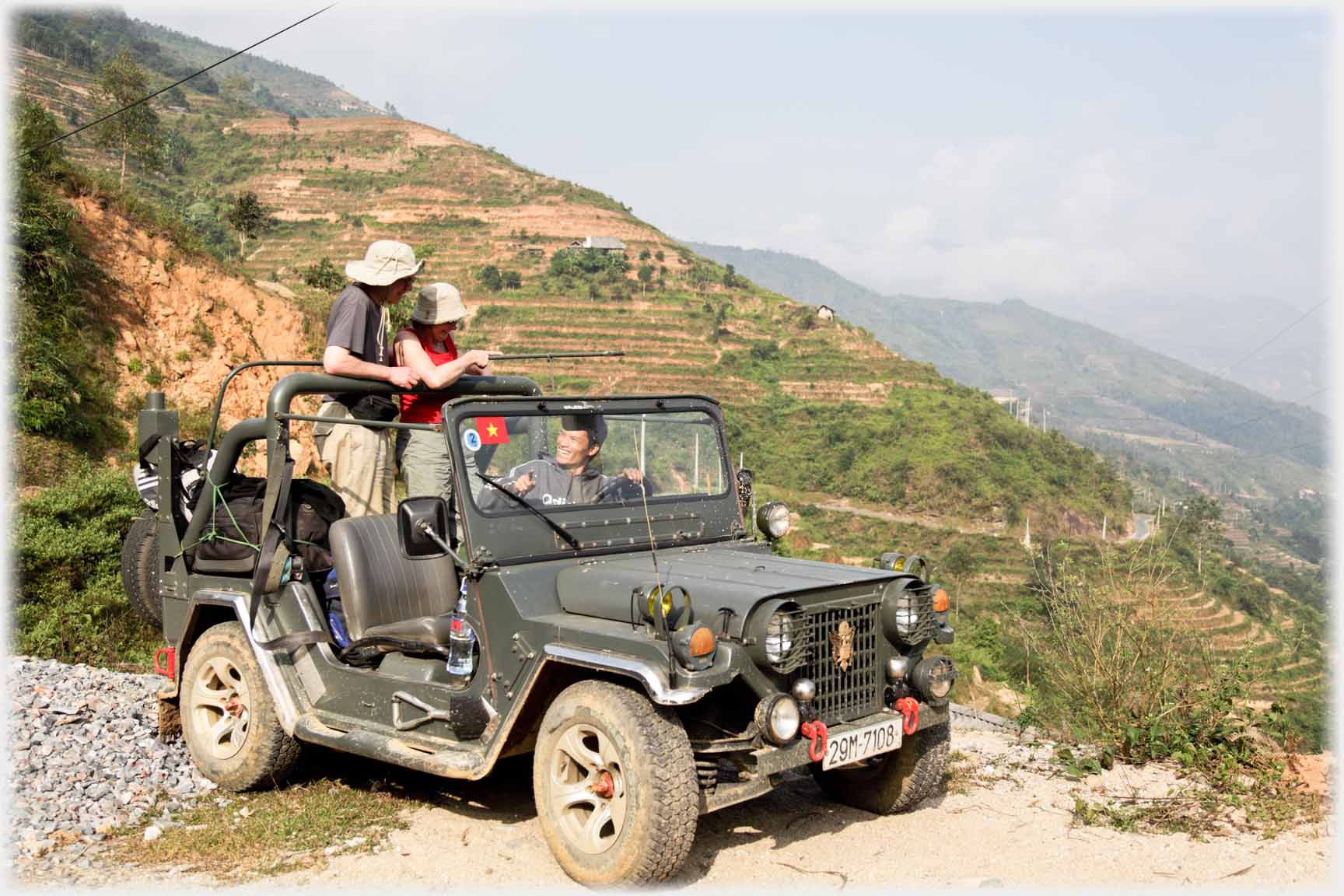 Two people standing up in back of a Jeep looking down valley.