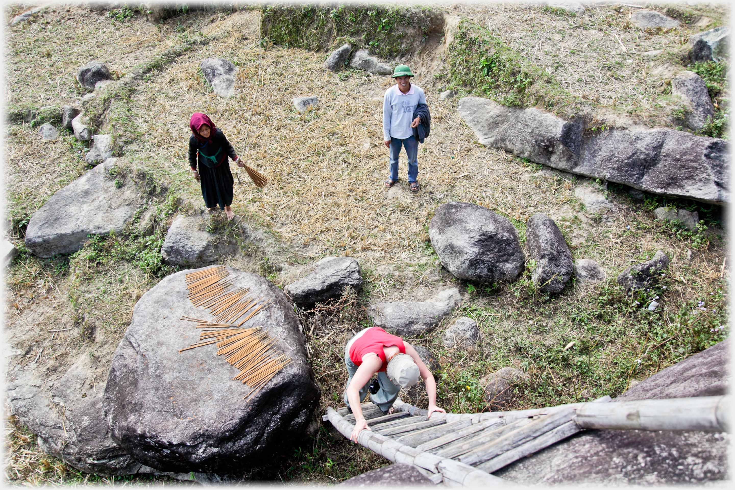 Looking down on person climbing ladder, man and woman with brush, watching from ground.