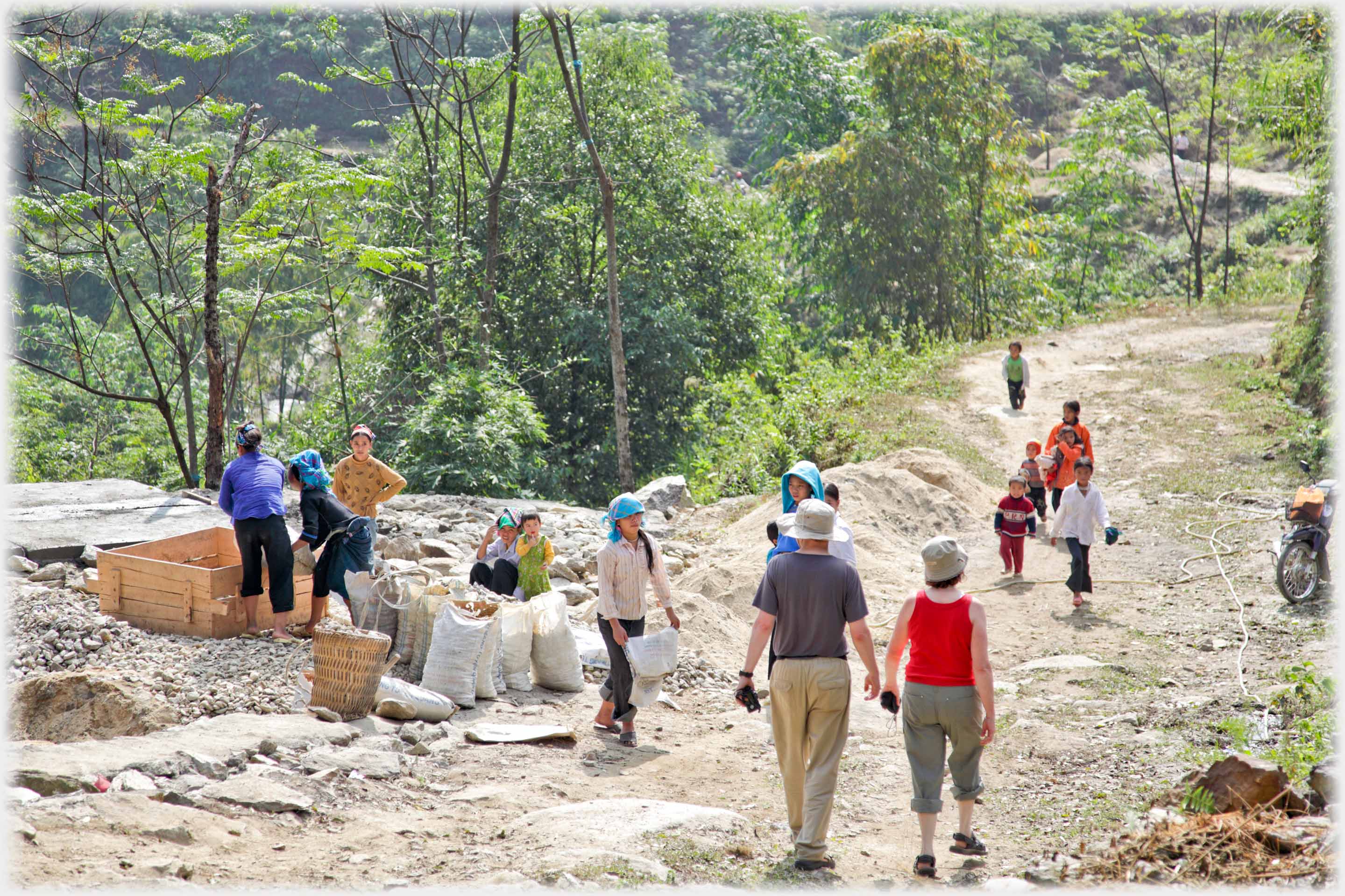 Two westeerners walking down track various workers and children watching.