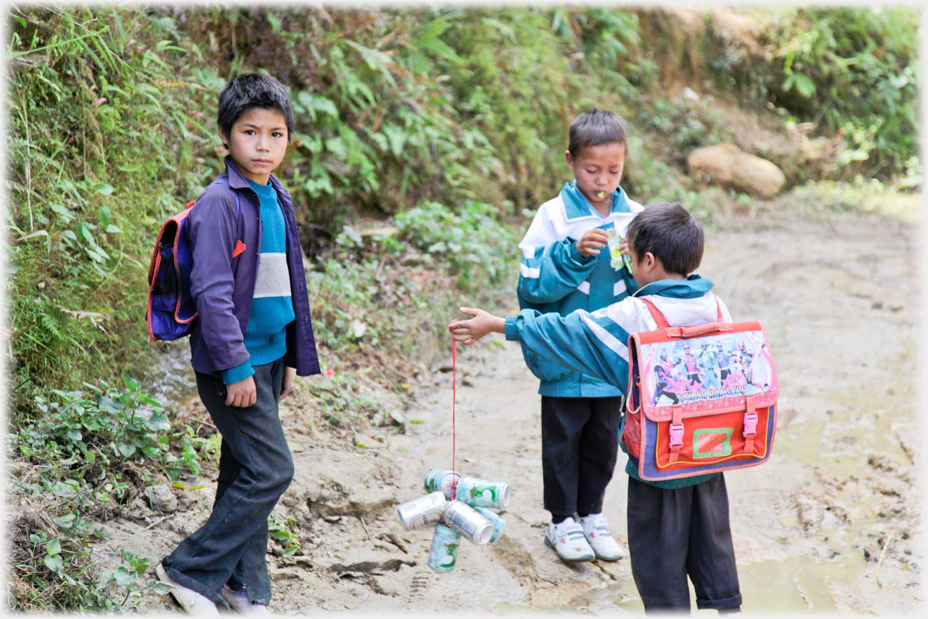 Boy looking at camera, two boys with tin cans on string.