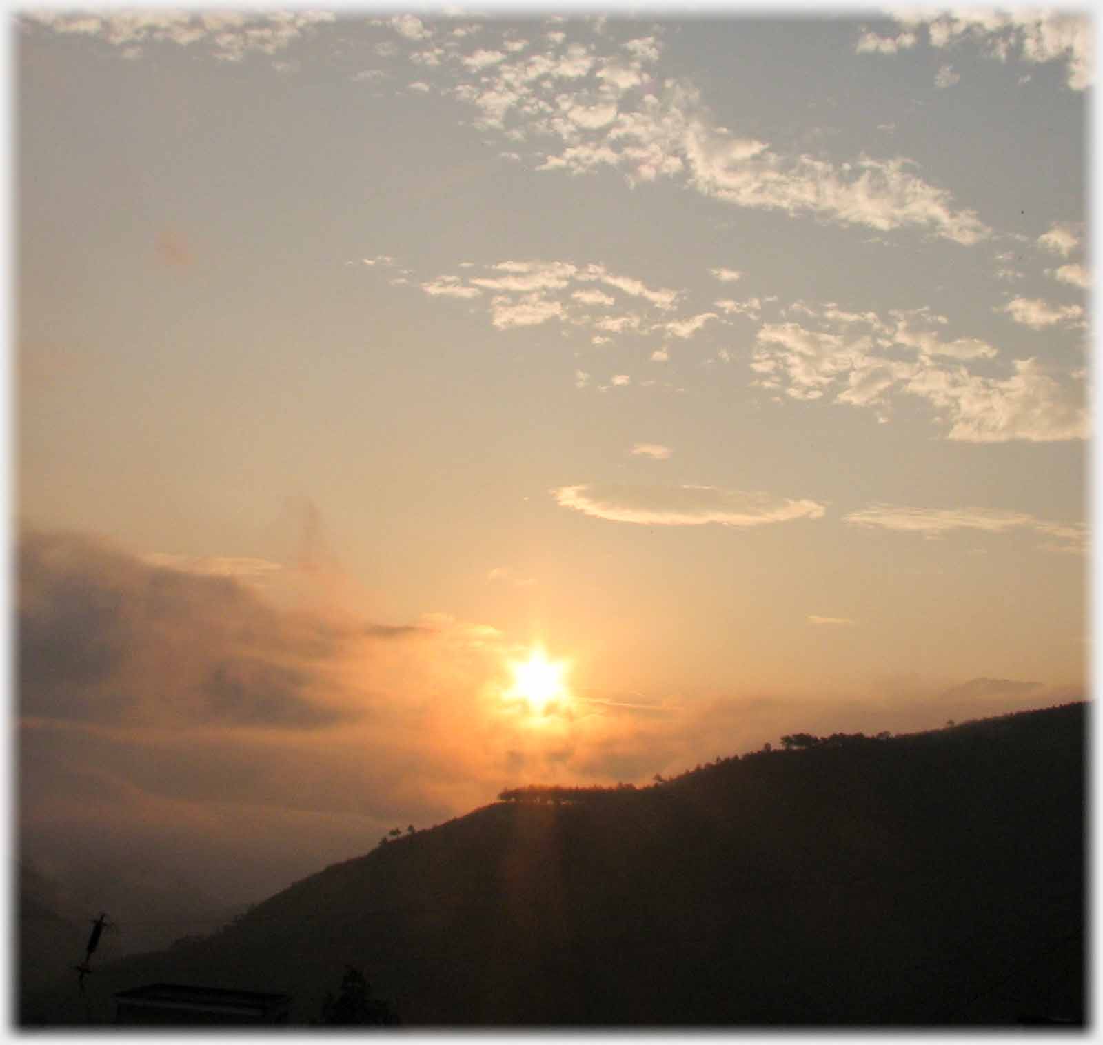 Sun rising just above clouds and hillside - it appears to be a six-sided star.