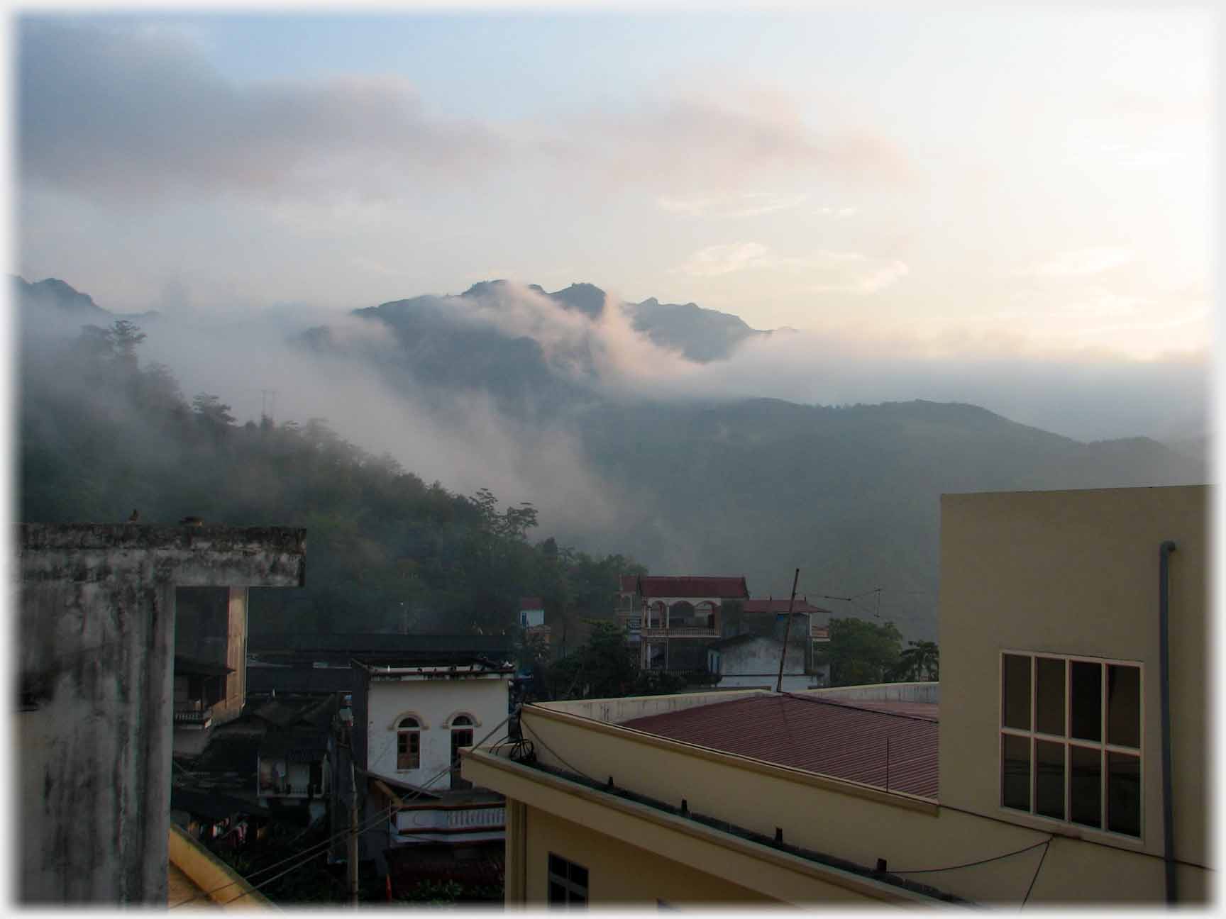 Modern buildings in foregroound, misty hills in distance.