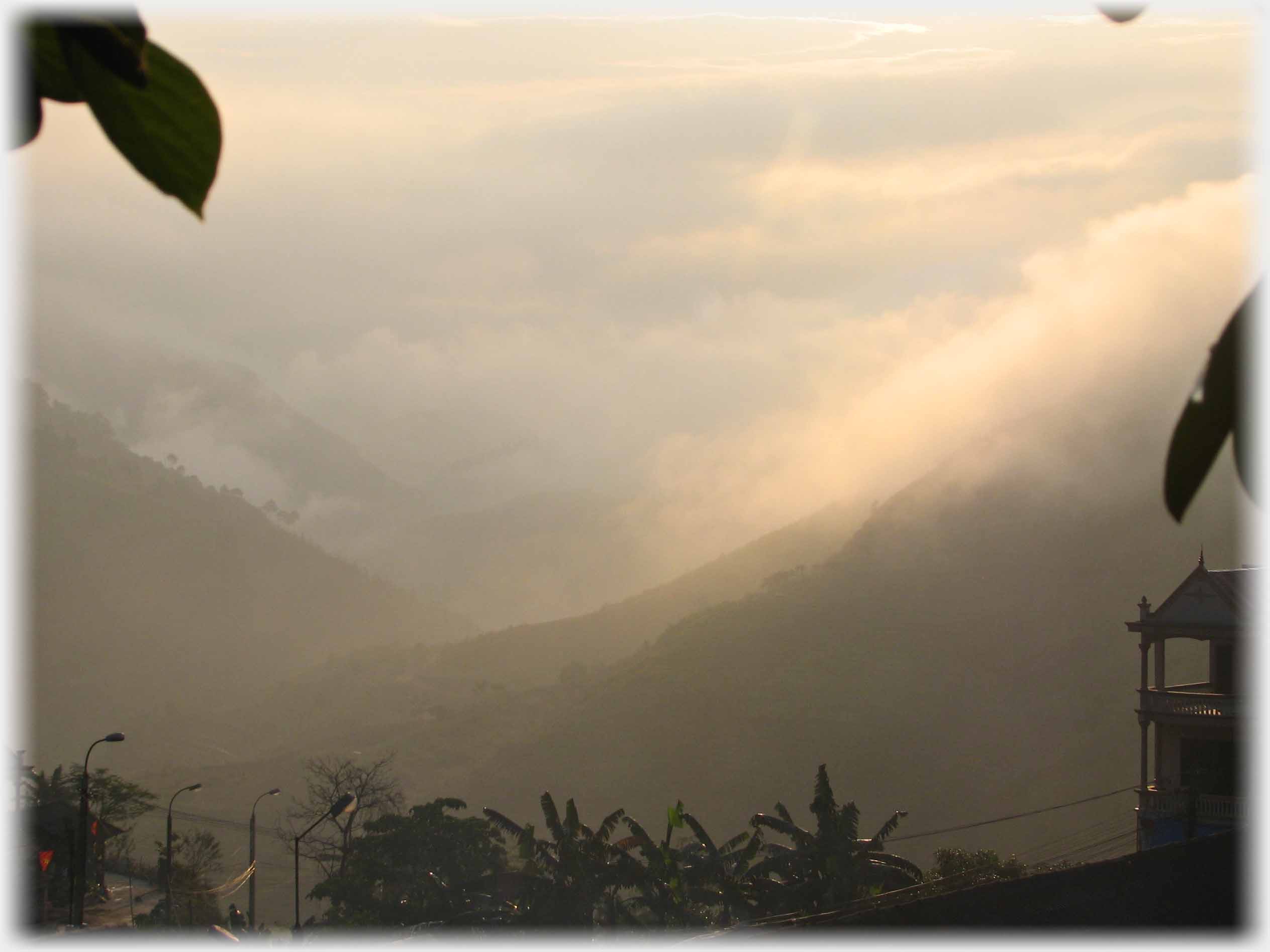Looking out of town, house to right, at mist on hillsides of valley, banana trees.