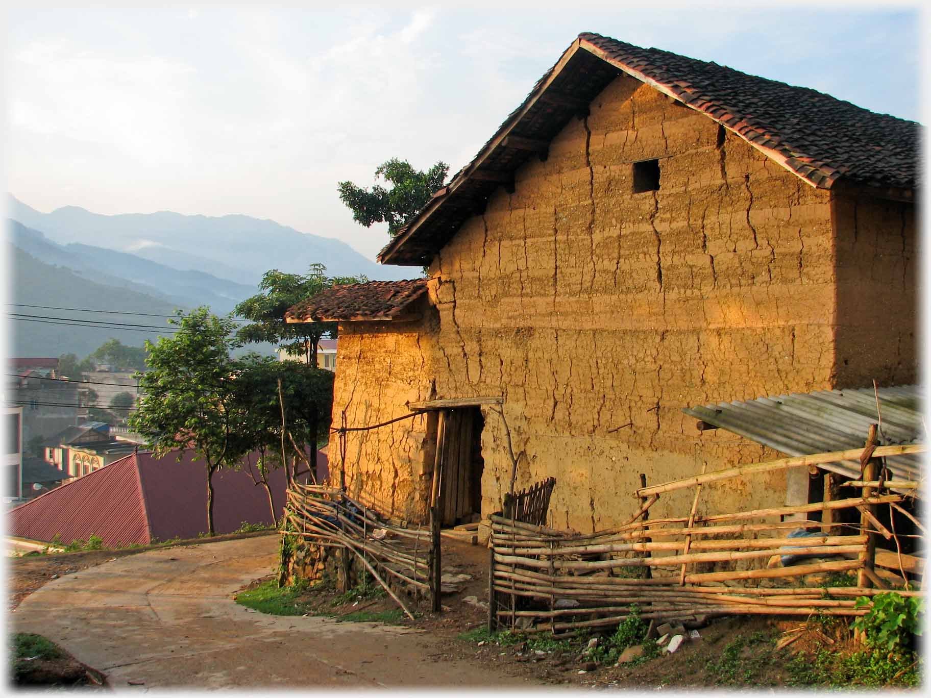 End wall of house showing layers of bricks cracking, wooden fence.