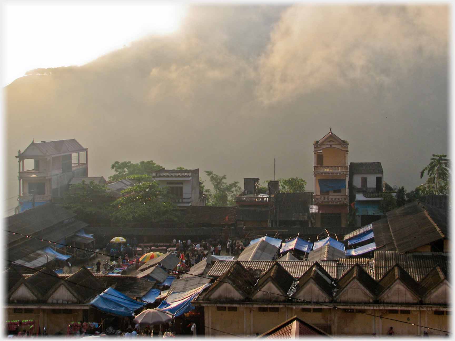 Complex pattern of roofs with hill and cloud behind.