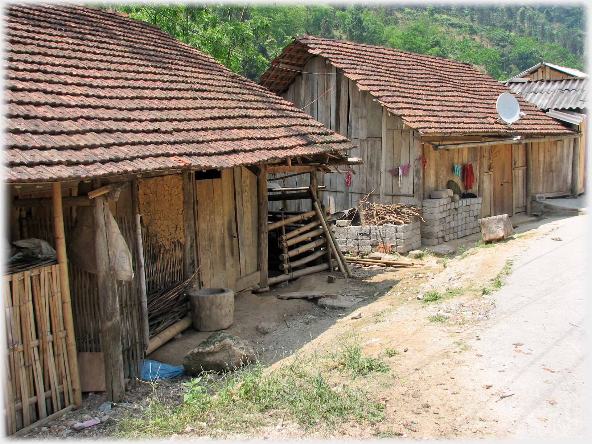 Two single story wooden and tiled houses at roadside.