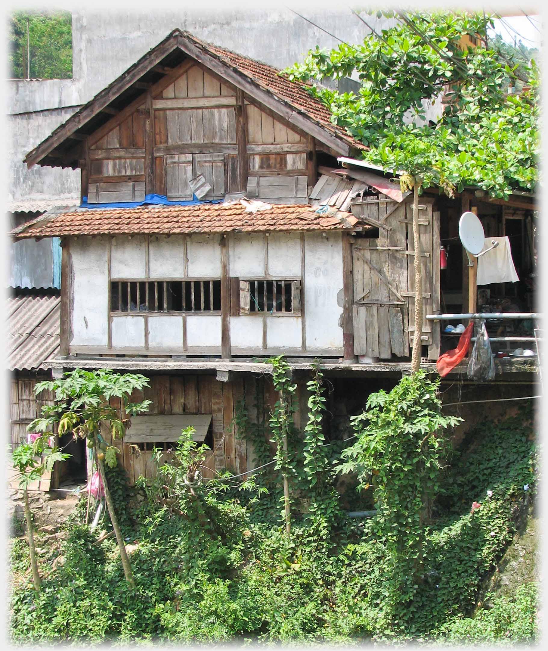 Three story wooden and tiled house on steep bank, middle story extending outwards.