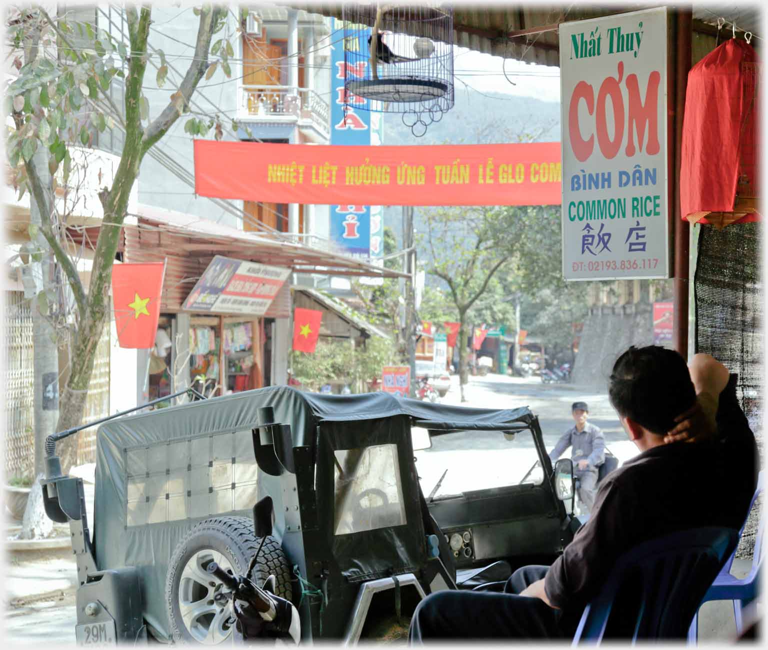 Man sitting looking down street, Jeep parked.