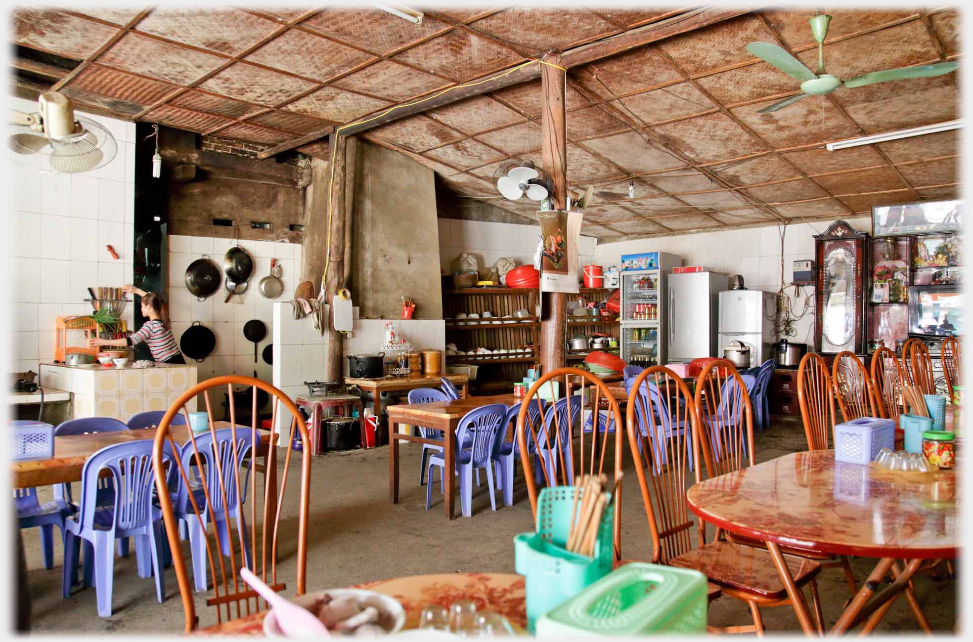 Inside cafe with utilitarian and plastic chairs, woman cooking.
