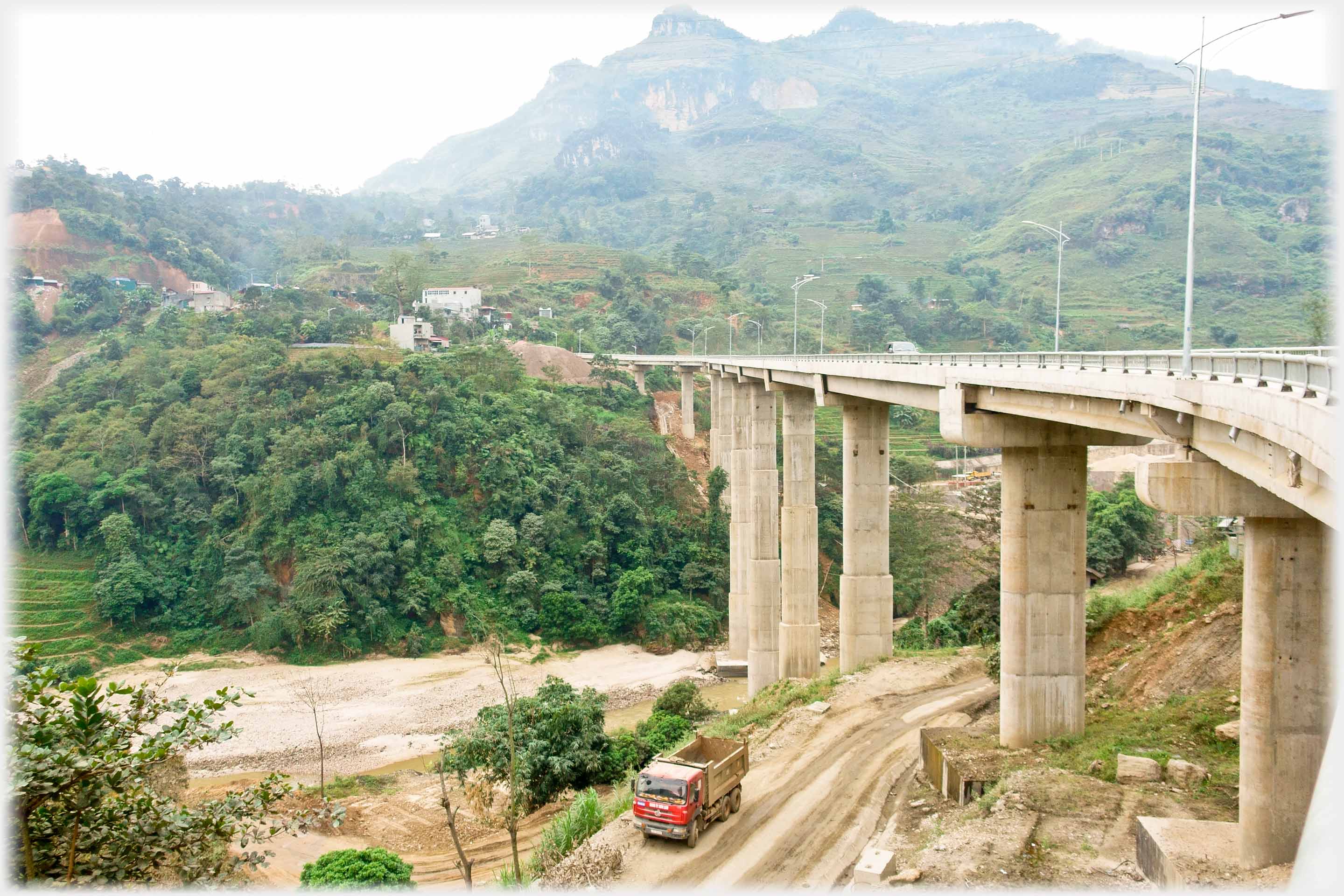 Bridge spanning valley with much disturbed ground and truck below.