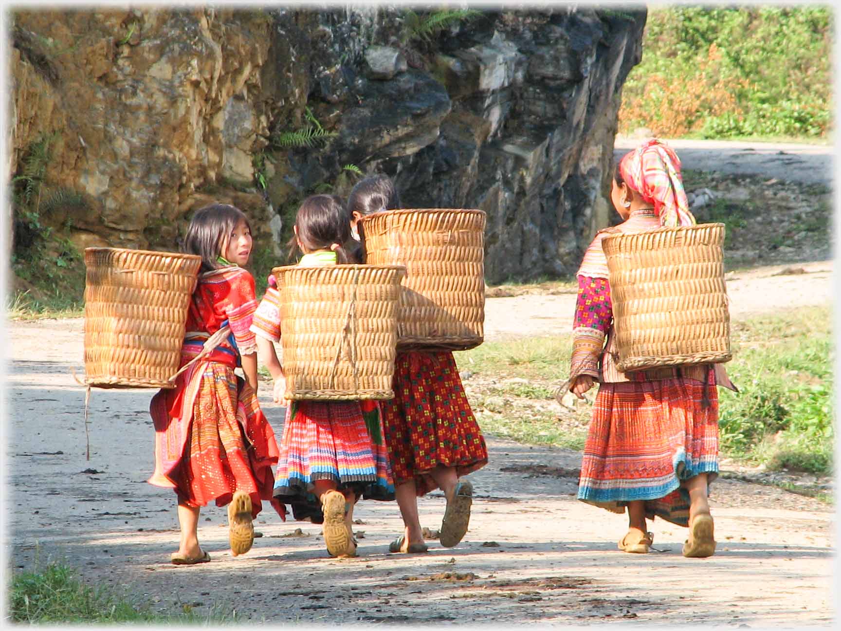 Woman and three girls walking away from camera, one girl looking back.