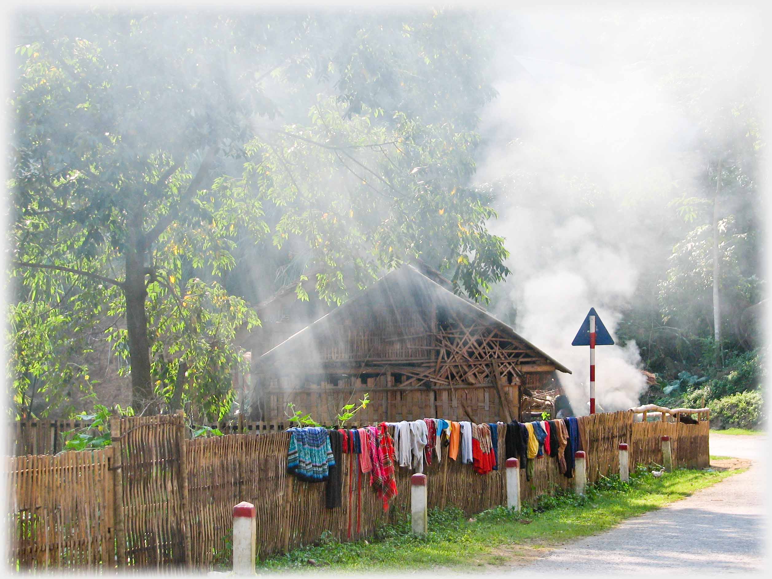 Shafts of sunlight onto house and bonfire with fence on which washing.