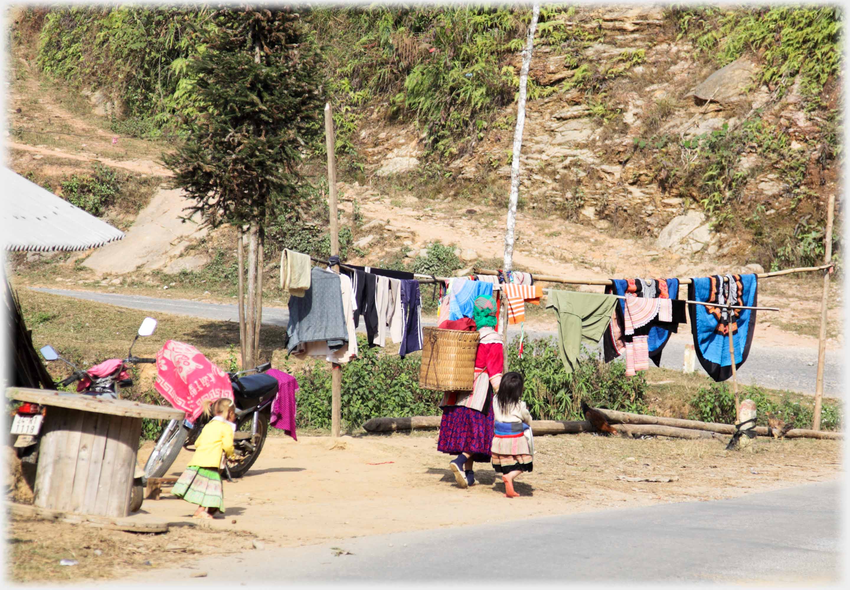 Line of washing with woman and small child in front of it by road.
