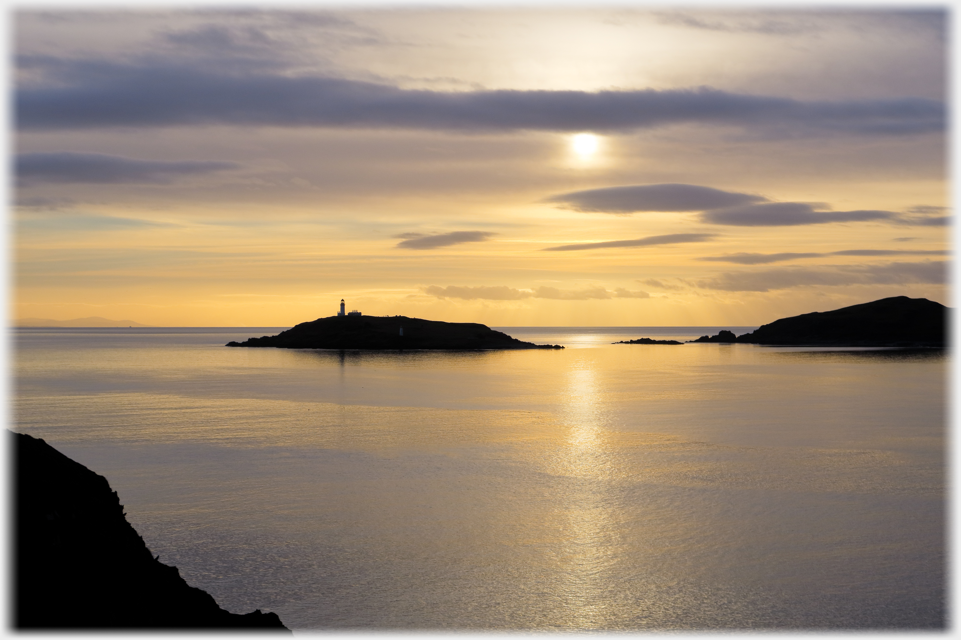 Sun reflected in sea beside island.