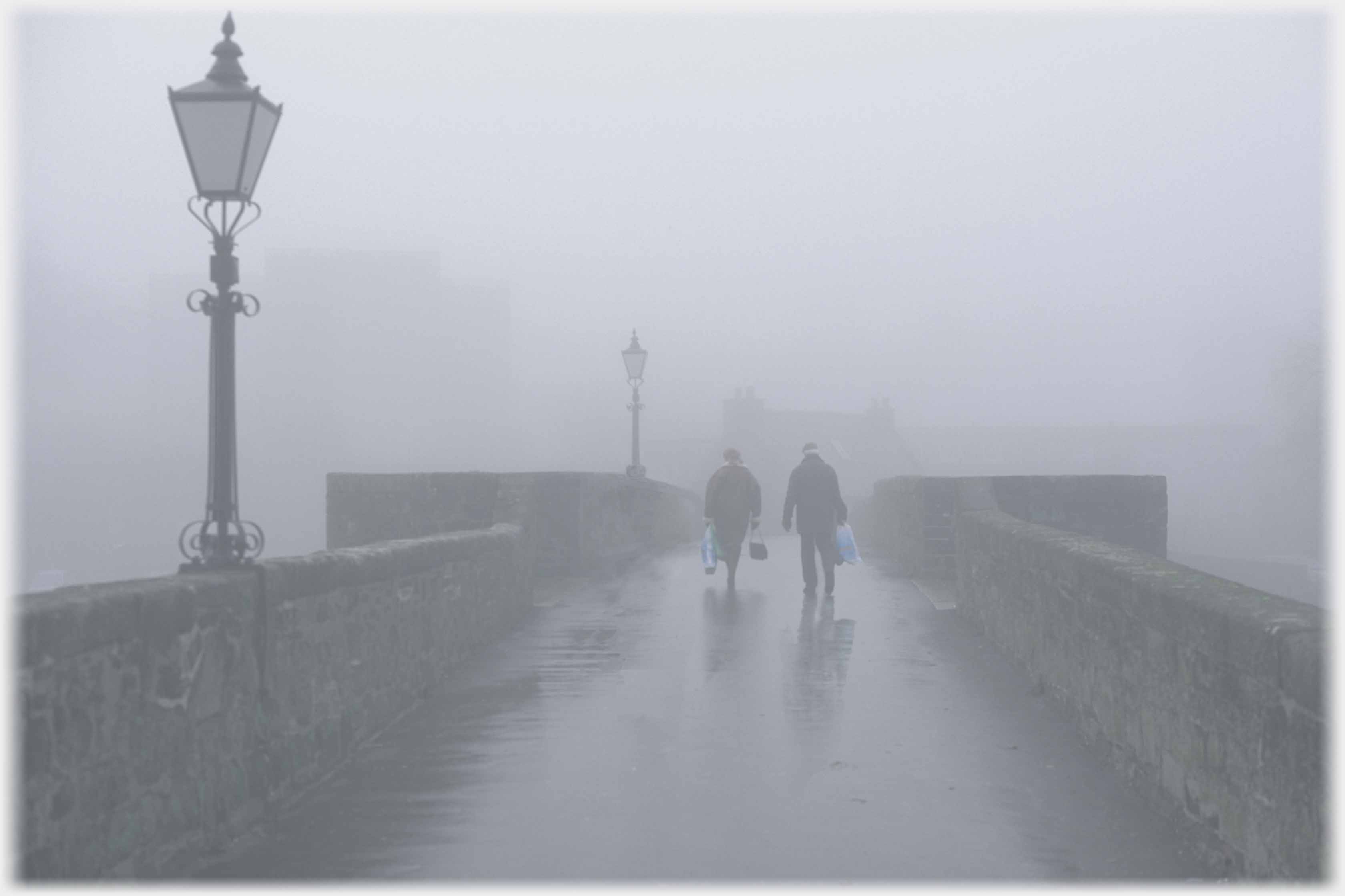 Two people walking over misty bridge.